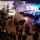 A crowd of people watches a band play on a brightly lit stage.